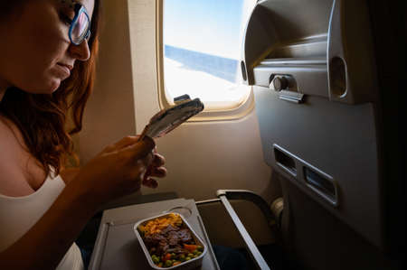 Caucasian woman flying in economy class and eating lunch from a tray table on board the plane.の写真素材