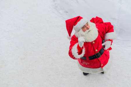 Top view on friendly santa claus actively gesturing and wishing merry christmas. An elderly man in a Santa costume stands on the snow outside and wishes a happy new year.の写真素材