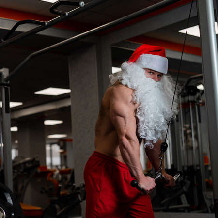Man in santa claus hat and red shorts posing at the gym.の写真素材