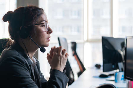 Portrait of woman in headset in frustration holds hands by face in office.の写真素材