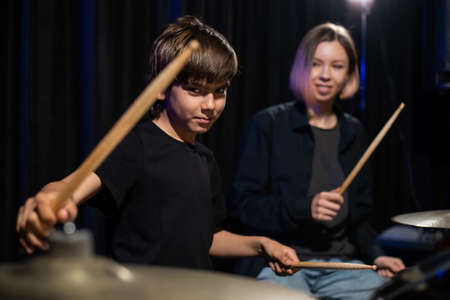 Young caucasian woman teaches a boy to play the drums in the studio on a black background. Music...