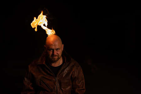A bald man in a leather jacket with a burning head grins.の写真素材