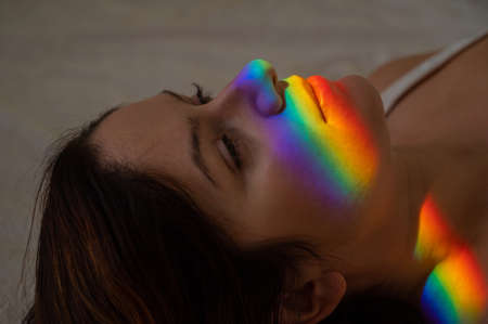 Close-up portrait of caucasian woman with ray of rainbow light on her face.