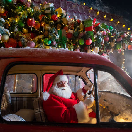 Portrait of santa claus driving a car loaded with a Christmas tree and giftsの写真素材