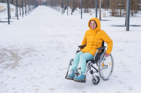 Caucasian woman with disabilities rides on a chair in the park in winter. Girl on a walk in a wheelchair.の写真素材