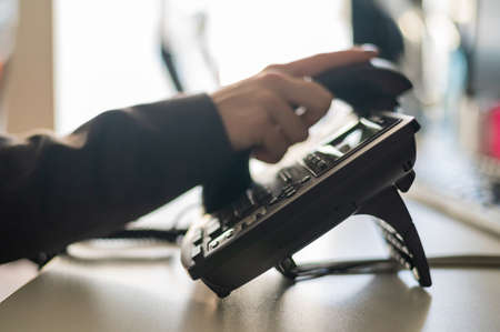 Close-up of the hand of a female office worker dialing a number on a landline phone. Faceless woman secretary calls on the phoneの写真素材