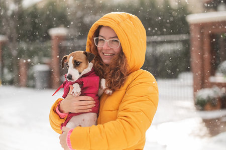 Caucasian woman hugging with dog while walking in winter. Jack Russell Terrier in a warm pink...