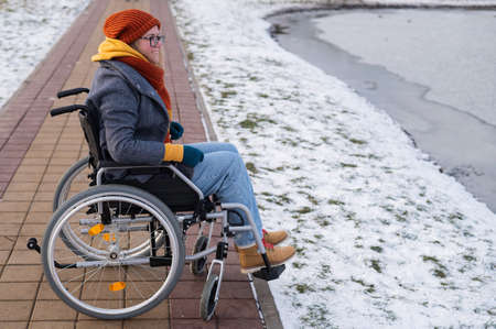 Caucasian woman in a wheelchair walks by the lake in winter.の写真素材