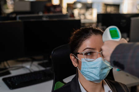 Doctor measures the temperature of an office worker with an infrared thermometer.