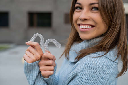 Caucasian woman with white smile holding transparent removable retainer. Bite correction device.