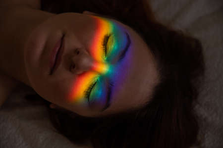 Close-up portrait of caucasian woman with ray of rainbow light on her face.
