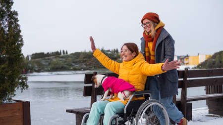 Caucasian woman driving her friend in a wheelchair along the lake in winter.