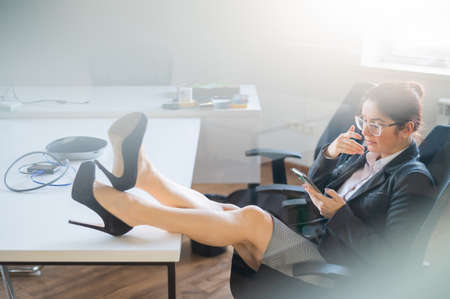 Business woman put feet on work desk and uses mobile phone in officeの写真素材