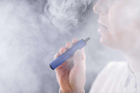 Caucasian woman smokes a disposable vape in the studio.の写真素材