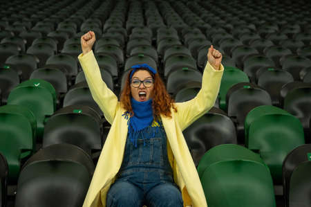 Caucasian woman cheers for a sports team at the stadium. The girl watches the match at the stadium alone.の写真素材