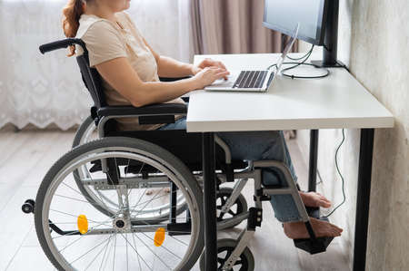 Caucasian woman in a wheelchair typing with a laptop from home. Remote work for people with...