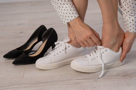 Close-up business woman takes off her shoes puts on white leather sneakers.