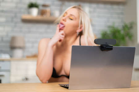 A girl in lingerie flirts on a webcam on a laptop. A woman works in the online sex industry
