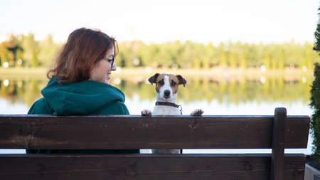Caucasian woman sits on a bench with a dog by the lake.の写真素材