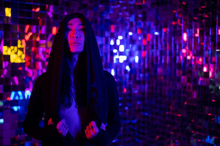 Close-up portrait of an androgenic model in a hood. Male transgender in studio with neon light.の写真素材