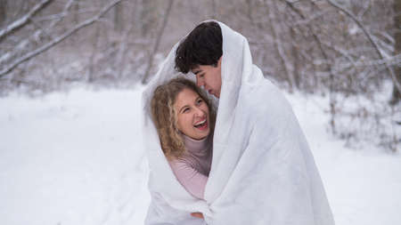 A young couple walks in the park in winter. The guy and the girl are kissing wrapped in a white...