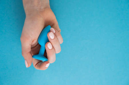 A woman is holding a blue anal plug on a blue background. Adult toy for alternative sexの写真素材