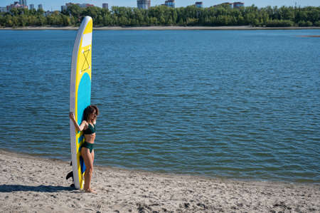 Caucasian woman walks along the beach and carries a sup board on the river in the city. Summer...