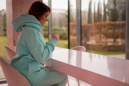 Caucasian red-haired woman eats ice cream with a plastic spoon while sitting alone in a cafe.