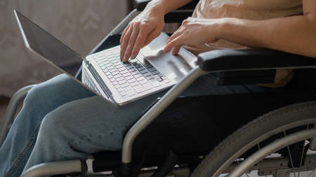 Caucasian woman in a wheelchair typing with a laptop from home. Remote work for people with disabilities.の写真素材
