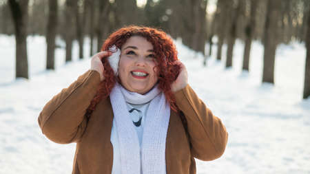 A plump woman listens to music in headphones while walking in the park in winter.の写真素材