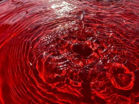Close-up rain drips on a red background and leaves circles on the water.の写真素材