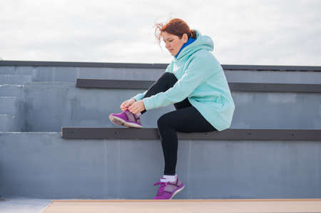 Caucasian woman in a hoodie tying her shoelaces before jogging.の写真素材