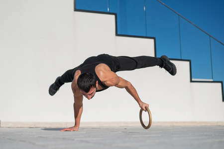 A man in black sportswear does an acrobatic handstand on a ring outdoors.の写真素材