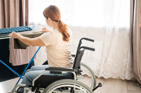 Caucasian woman in a wheelchair hangs wet laundry on a dryer.の写真素材
