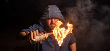 The man in the hood is holding a burning bottle. Molotov cocktail.の写真素材