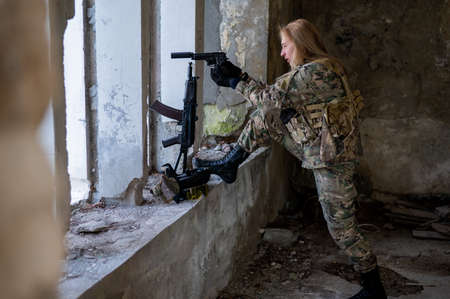 A woman in an army uniform aims to shoot a firearm in an abandoned building.