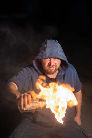 The man in the hood is holding a burning bottle. Molotov cocktail.
