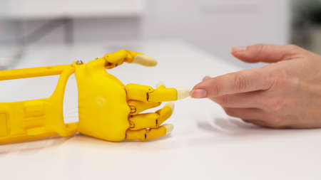 Womans hand and a plastic hand prosthesis for a child on a white background.