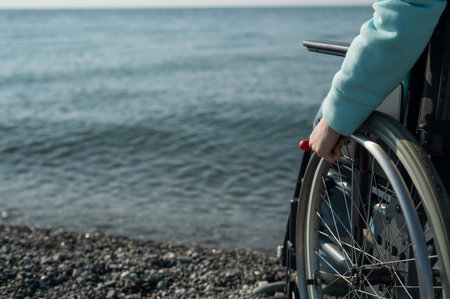 Caucasian woman in a wheelchair on the seashore. Close-up of female hands.