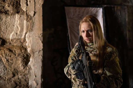 Caucasian woman in army uniform holding a machine gun and standing near an open coffin.