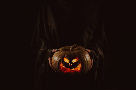The witch is holding a pumpkin jack o lantern glowing in the dark. Halloween.の写真素材