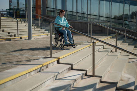 A caucasian woman in a wheelchair cannot go down stairs without a ramp. Hard to access environment.の写真素材