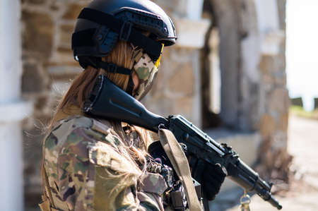 Caucasian woman in a protective suit with a machine gun. A female soldier in a camouflage uniform...