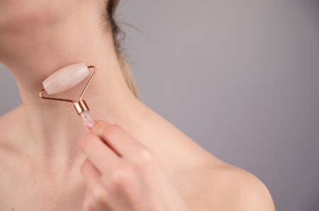 Close-up portrait of a woman using a quartz roller massager for an alternative fight against wrinkles on her neck. Smoothing of the rings of venus.の写真素材