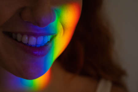 Close-up portrait of smiling woman with ray of rainbow light on her face.の写真素材