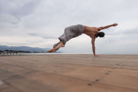 Shirtless caucasian man doing backflip on pebble beach.
