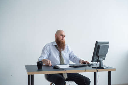Problems for the office worker. A bald man in a white shirt sits at a desk with a computer and is stressed because of failure. A nervous breakdown.の写真素材