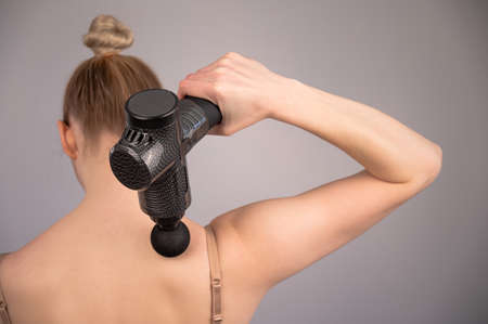 Caucasian woman giving herself a back massage with a gun.の写真素材