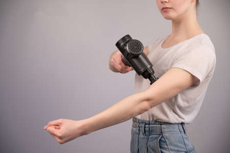 Caucasian woman uses a massager gun for pain in the muscles of the arm.の写真素材