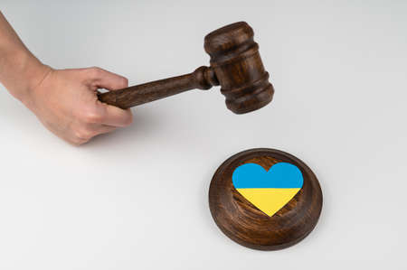 Woman hitting the judges gavel on the heart with the flag of Ukraine on a white background.の写真素材
